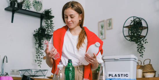 A woman wearing a sweater, standing in her kitchen looking and disposing of plastic.